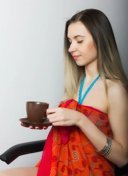 Beautiful  young woman in bikini and pareo sitting on a chair and drinking coffee in brown cup