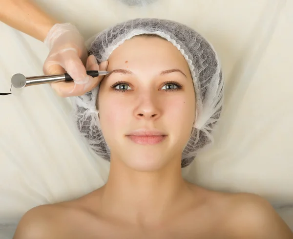 Beautician examining the face of a young female client at spa salon. Permanent makeup, tattoo in a beauty salon. Professional consultation