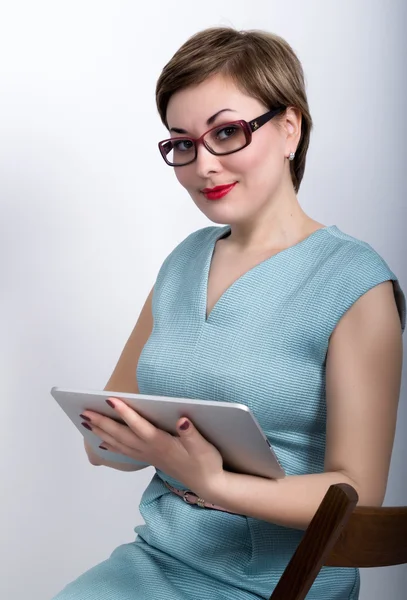 Beautiful asian woman in a business suit and glasses holds a pc tablet in the hands of and siting on a cheir