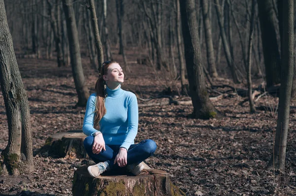 Beautiful girl blonde sits in lotus pose in the middle of the forest in the spring