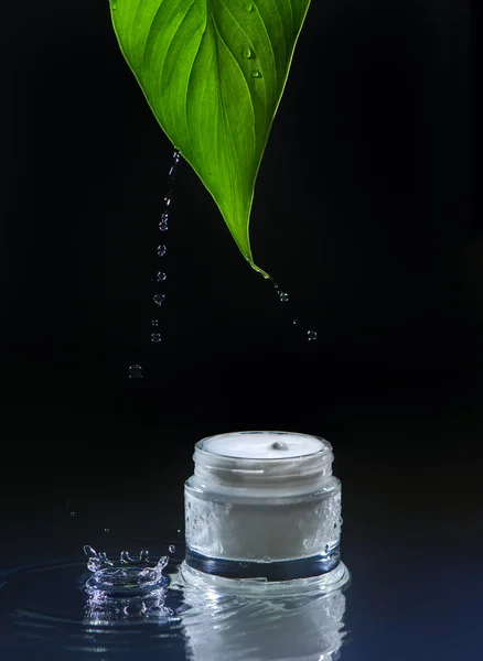 Moisturizing cream for dry skin, black water background, green leaf, splash