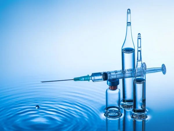 Medical ampoules and syringe on blue water background with splash and drops