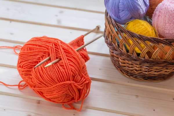 Orange knitting wool and wooden needles with colorful yarn balls on background