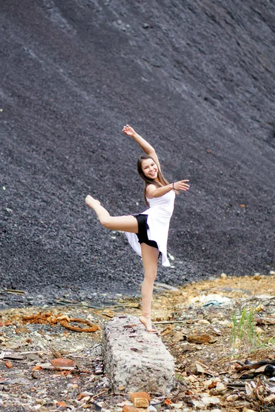 Beautiful girl in the gymnastic pose with a smile on his face performs an exercise on landfill