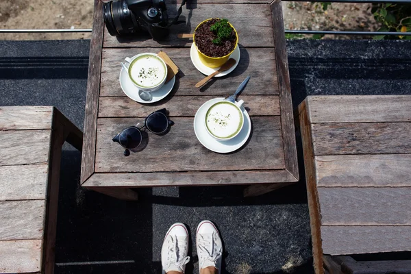 Wooden table with green tea lat, white gym shoes, the girl at a table with food, camera on a table, a dessert on a table