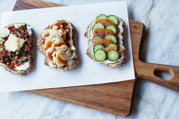 Bruschettas with red fish and a cucumber, banana with peanut paste and almonds, tomato with a cucumber, bruschettas on a wooden board, tasty food