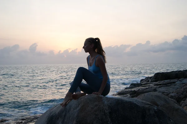 The beautiful girl sitting on stones and looking in a distance, the girl at sunset to meditate in silence, beautiful telo.concept .Siluet lonely girl sitting on the precipice of a cliff at sunset.