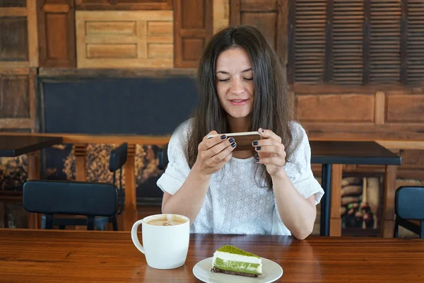 The young girl in cafe, photographs on phone food, a cup of tea, coffee, cake green