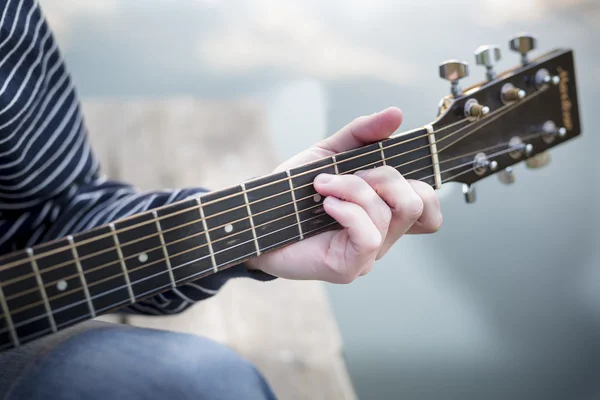 Young guy playing a guitar at sunset on river.Close up his hands and guitar neck .