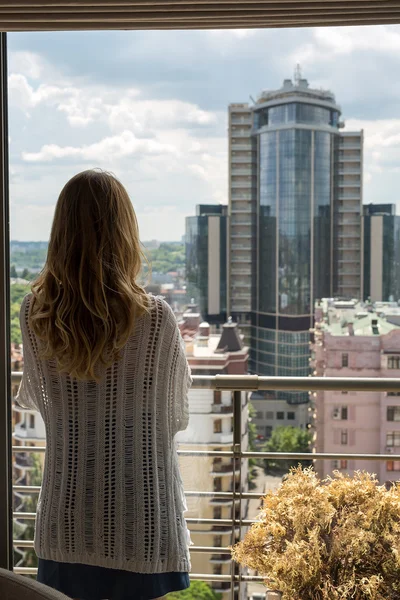 Young beautiful blond girl standing with her back in the window and sad
