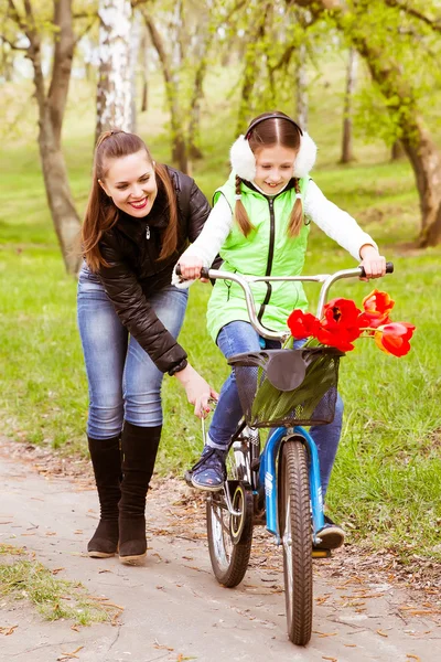 Happy mother teaches his daughter to ride a bike. Mother holds daughter from falling