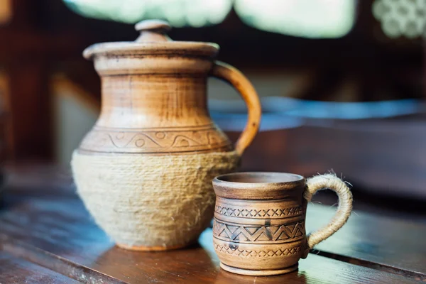 Pitcher and Cup of red clay with Ukrainian ornament on the wooden table