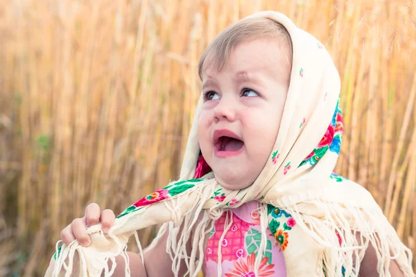 Little girl in scarf stands in the middle of the field and cries. Orphans, social problems.