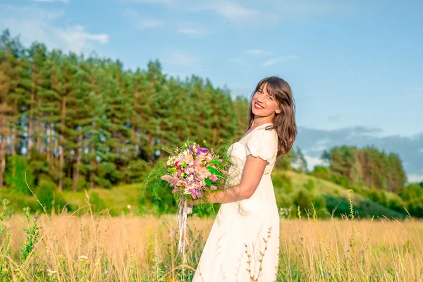 Young woman with a bouquet in hand spinning and dancing in the forest and fields