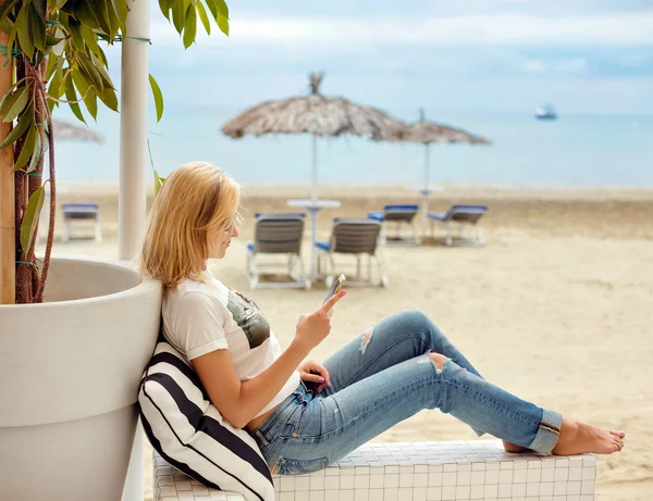 Slim blonde girl in jeans sitting and looking at phone on the ba