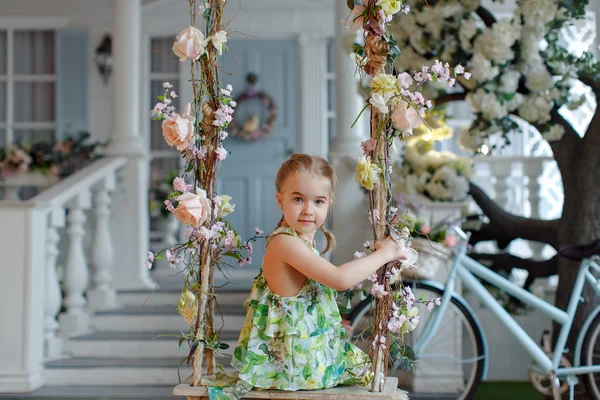 Cute little girl in a green dress sitting on swings decorated wi