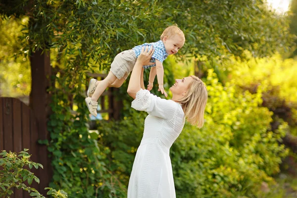 Mom blonde in white dress lifts up the little boy and laughing a