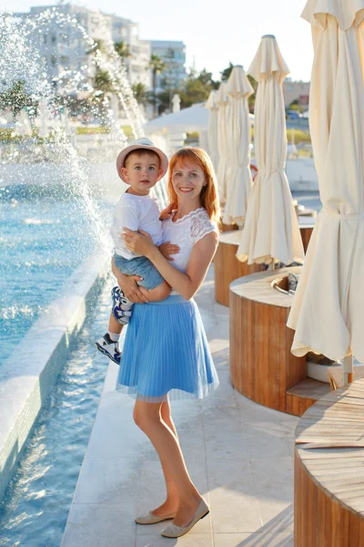 Young slim mother in a blue skirt holding her son hands and laug