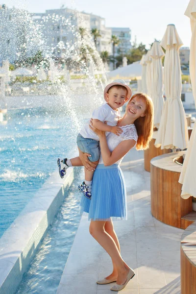 Young slim mother in a blue skirt holding her son hands and laug