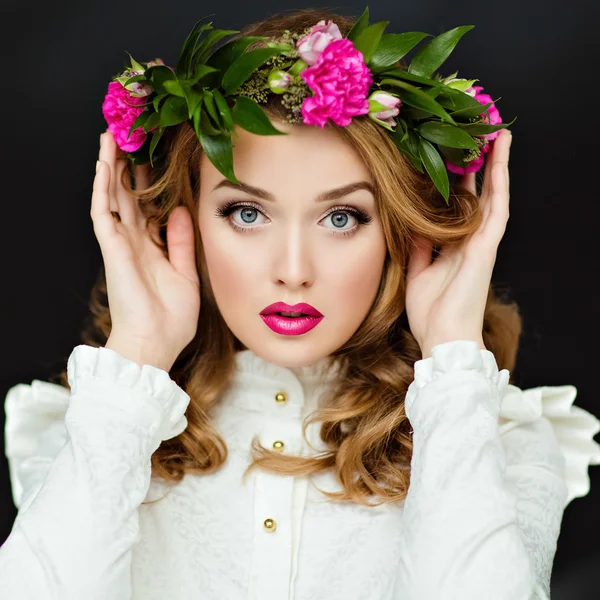 Portrait of a beautiful sensual glamorous yellow-haired girl in a white blouse with a wreath of flowers on his head, in the Studio on a dark background, close up