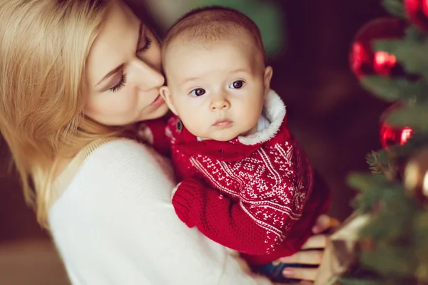 Mom blonde in white sweater kisses little boy the kid in the red