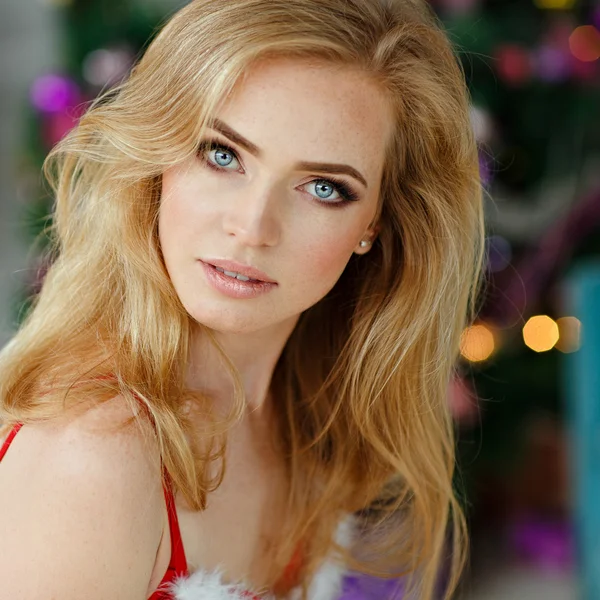 Portrait of sensual blond girl with freckles, against a background of Christmas trees and lights in the interior, close-up