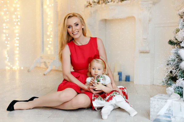 Mother in red dress smiles and holds a lovely baby girl blonde w