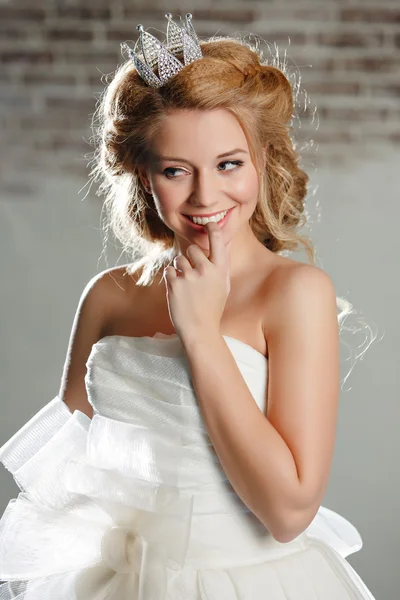 Close-up portrait of a smiling young blonde woman with full lips, wearing a white dress and a crown on her head, like a princess, looking away coyly