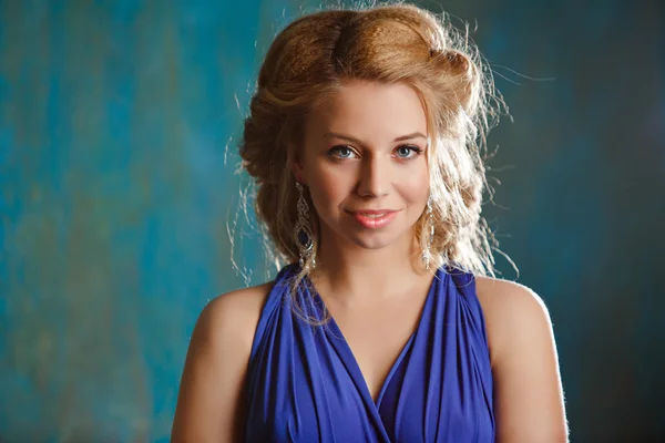 Portrait of charming girl with thick blond hair and blue eyesin a blue dress dress in the studio, close-up