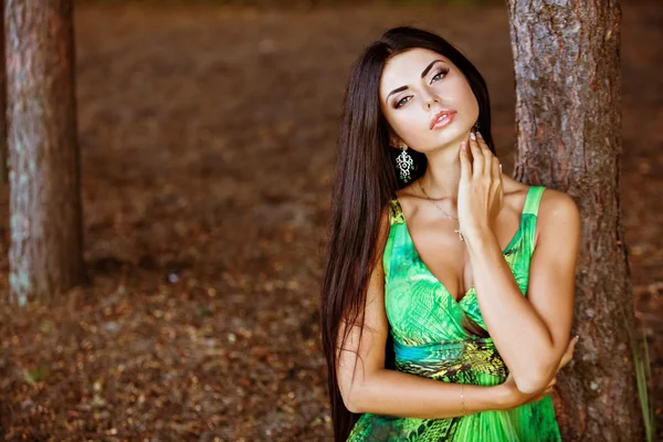 Portrait of a sexy sensual very beautiful brunette girl with long hair in a green dress in nature, close up