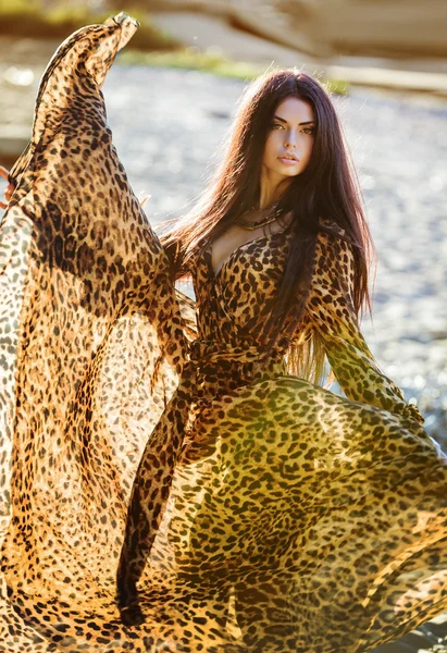Sexy sensual beautiful brunette girl with long hair in leopard print dress, dancing on the sand