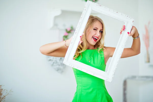 Beautiful blonde girl in a green dress holding frame and winks