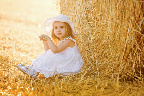 Adorable little girl in a white dress and white hat on is sittin