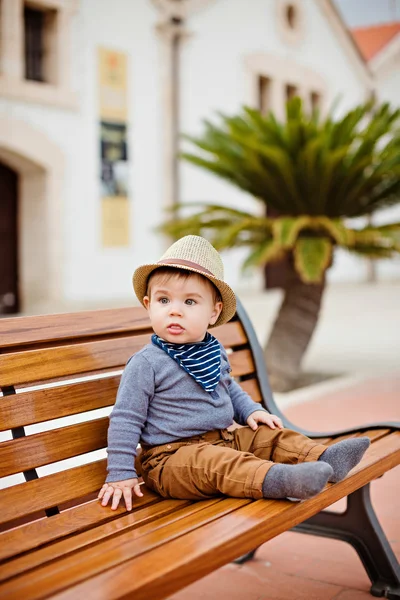 Little adorable baby boy in a straw hat and brown pants sitting