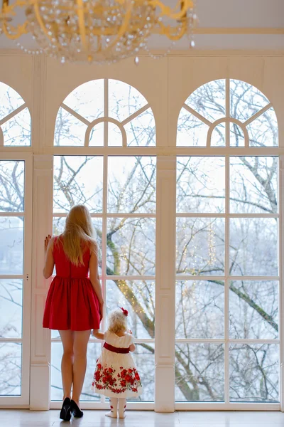 Charming blonde girl in a red dress holding the hand of her daug