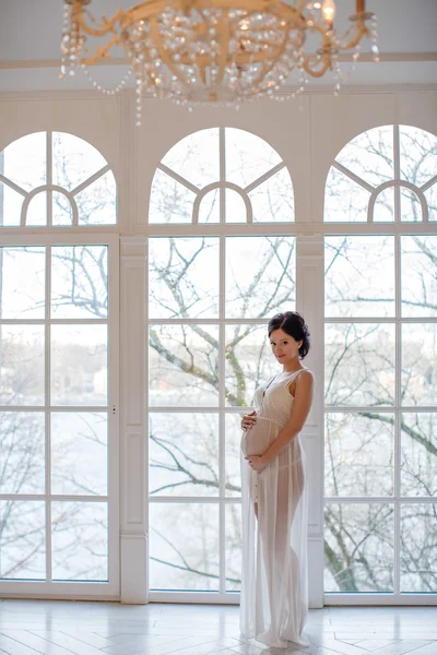 Portrait of a girl pregnant brunette in a white transparent dres