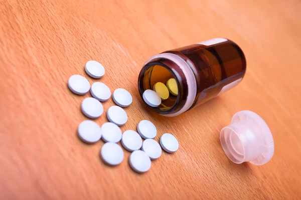 Bunch of blue pills with a bottle and a cap on an old vintage wo