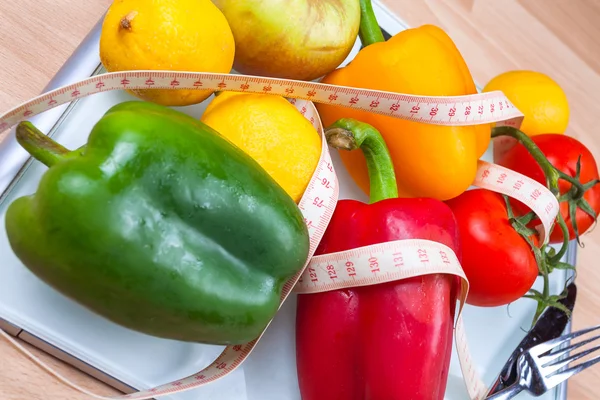 Peppers, tomatoes, apple and lemons on a scale with cutlery and t