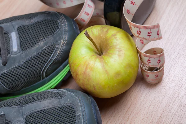 Worn out trainers, dumbbell, tape measure and an apple.