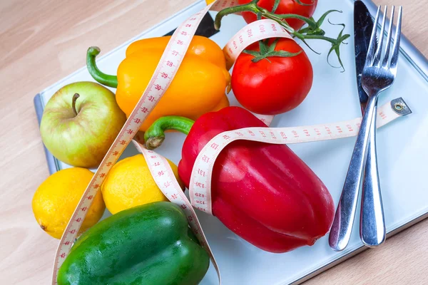 Peppers, tomatoes, apple and lemons on a scale with cutlery and t