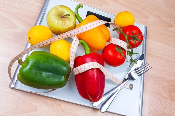 Peppers, tomatoes, apple and lemons on a scale with cutlery and t