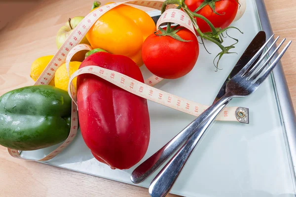 Peppers, tomatoes, apple and lemons on a scale with cutlery and