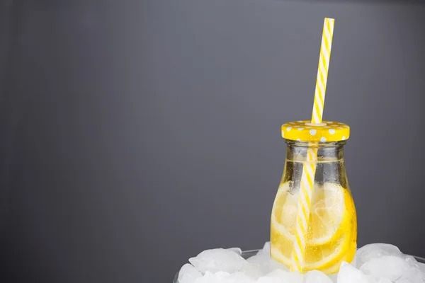 Lemonade drink in trendy bottle with straw on ice.