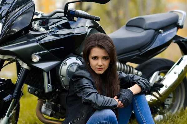 Biker girl sits near the motorbike outdoors on the road