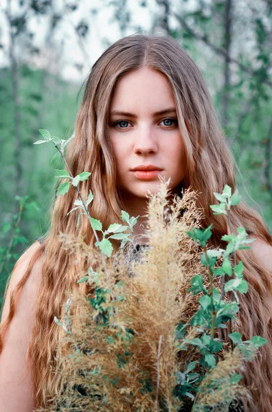 Embodiment.Spring time.Awesome,excellent,beautiful,nice girl with long,straight, little bit curly light hair with flowers outdoors in greenery in summer.Stunning girl,calm and serious girl with serious face,look,eyesight with bouquet of many flowers.