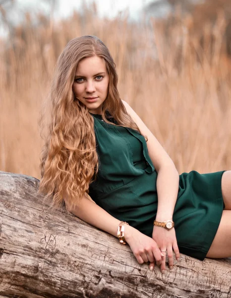Attractive,serious,impudent,bitchy girl,woman with curly long hair.Summer.Beautiful girl,beautiful,attractive,nice,pretty,lovely,cute,serious,impudent,mysterious,bitchy girl,woman with curly long hair,green dress lay on old,decrepit,log outdoors.