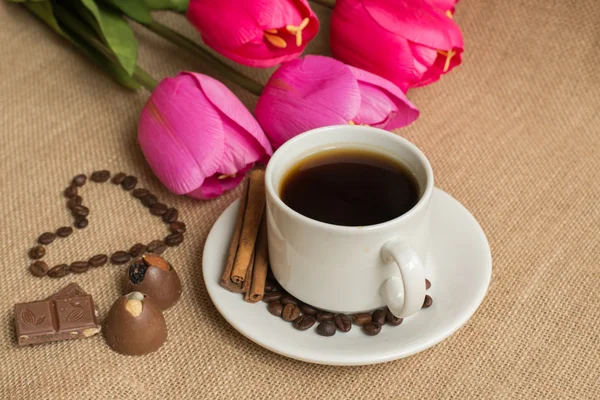 Coffee  cup with coffee beans on burlap and pink tulips