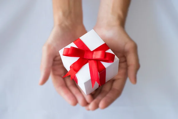 The man hands holding white gift box with red ribbon