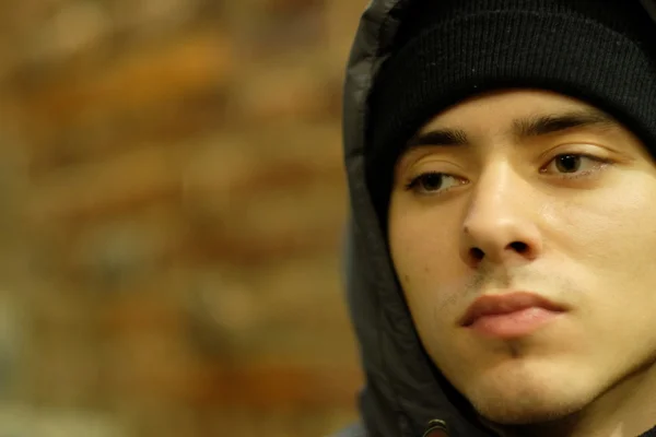 Portrait of a twenty-year-old boy in the hood on the brown brick wall background