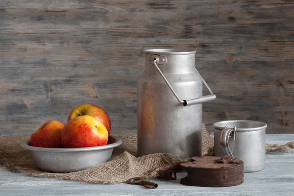 A set of aluminum cookware, rusted padlock and red apples on a wooden table